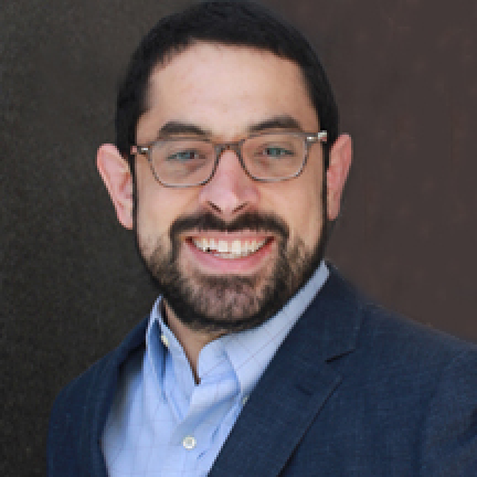 Headshot of Michael Sofis. They wear a blue suit against a brown background.