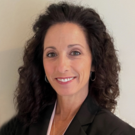 Headshot of Pamela O'Sullivan who is smiling at the camera. She has dark brown hair and is wearing a black suit.