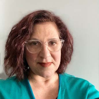 The image shows a headshot of Susan Lange with medium length red hair, slightly smiling. They have glasses with a clear frame and are wearing a teal top.